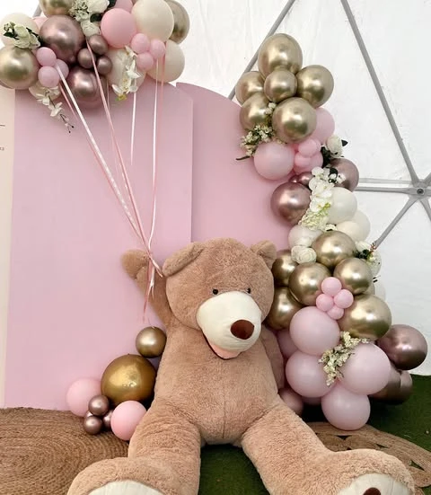 A giant teddy bear prop sitting next to a pink backdrop at a 'We can bearly wait' baby shower.