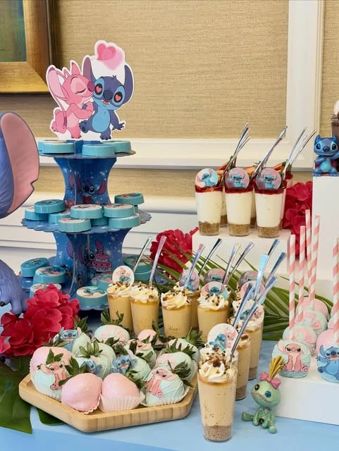 A dessert table with Stitch and Angel themed treats like decorated strawberries and dessert cups.