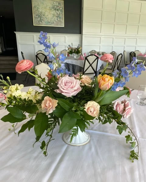A spring floral centerpiece with pink roses and blue delphinium on a white tablecloth.