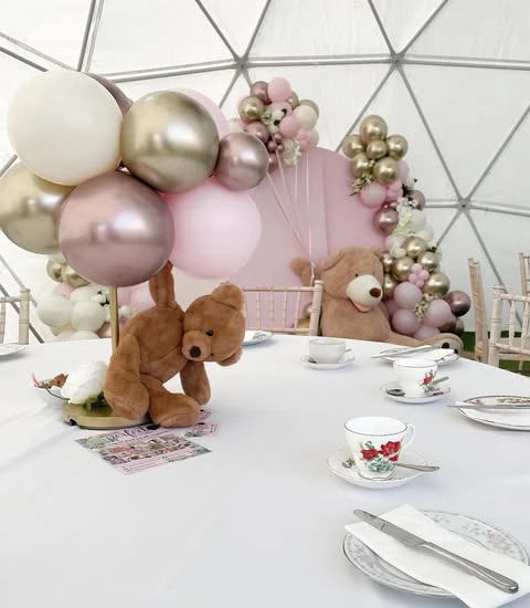 A teddy bear baby shower centerpiece with a small bear holding a bouquet of pink and metallic balloons.