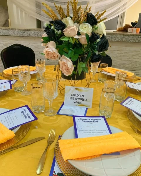A retirement party table centerpiece with black and pink roses in a modern gold vase.