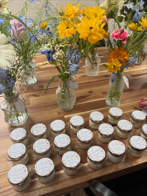 Wildflower-themed baby shower favors and small flower arrangements on a wooden table.