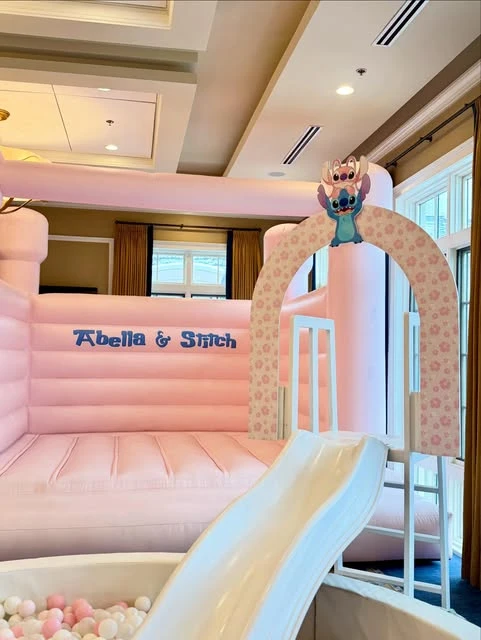 A pink bouncy castle with a slide and ball pit, decorated for a Stitch and Angel birthday party.