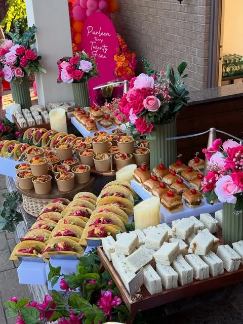 An abundant baby shower food table setup with platters of mini tacos, sliders, and finger sandwiches on tiered stands.