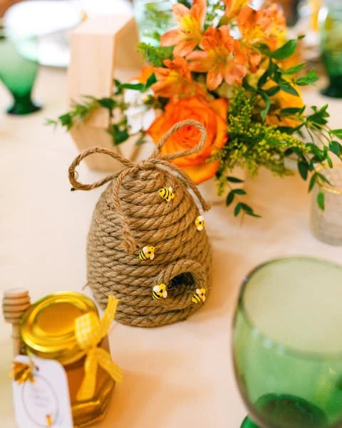 A close-up of a DIY twine beehive centerpiece decoration with small bee charms.