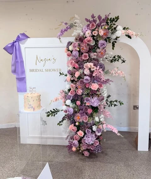 White arched backdrop for a spring bridal shower decorated with a lush cascade of purple and pink flowers.
