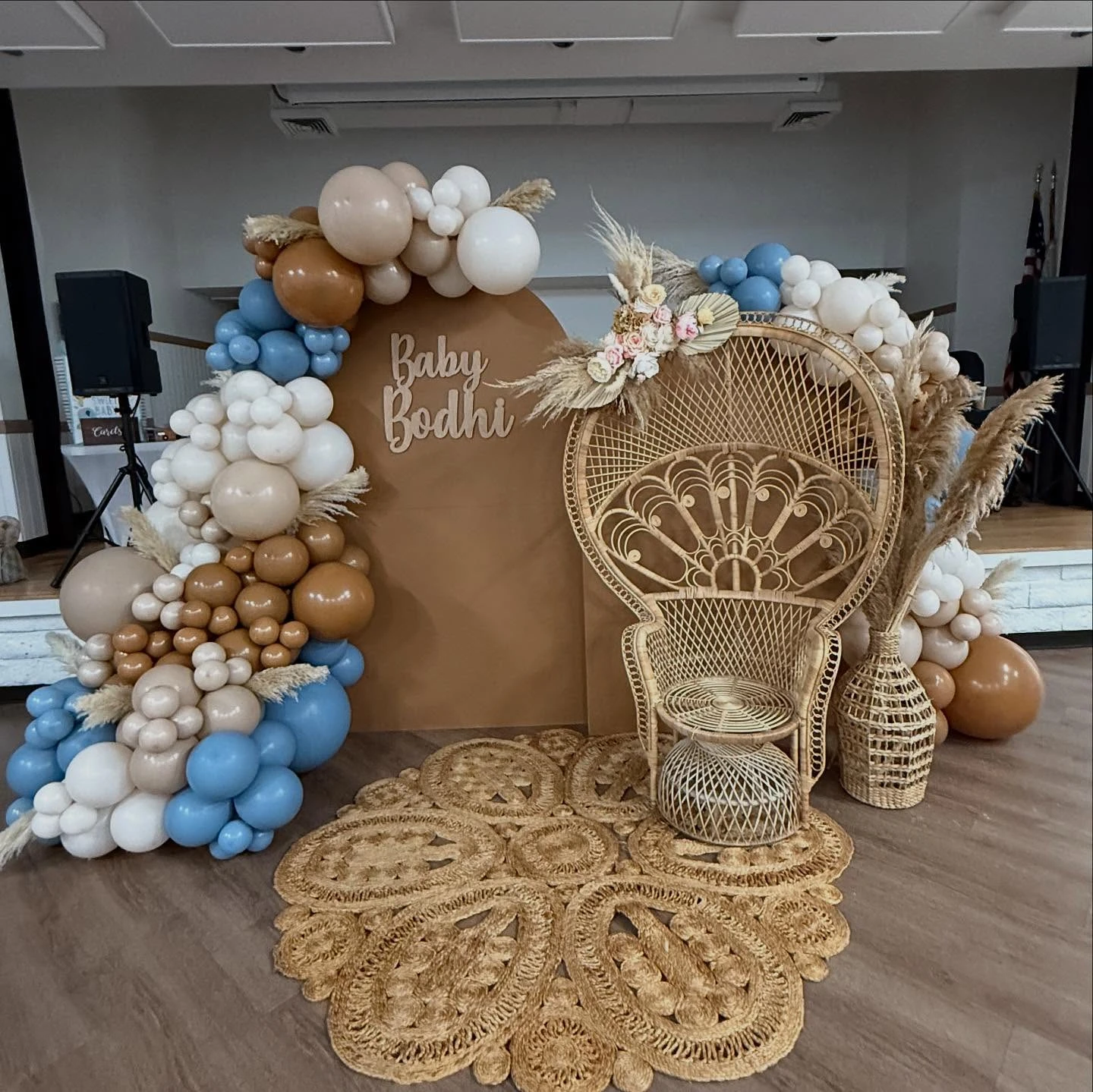 Boho baby shower photo backdrop with a peacock chair and an organic balloon arch in brown, tan, and blue.