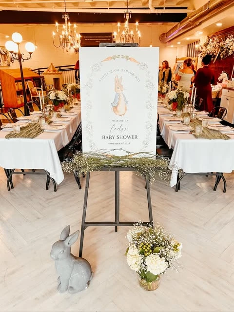 Peter Rabbit baby shower welcome sign on an easel between two long dining tables.