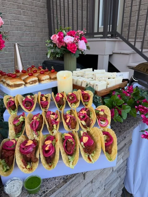 A of mini tacos with pickled onions and beef sliders on white serving platters for a party food table.