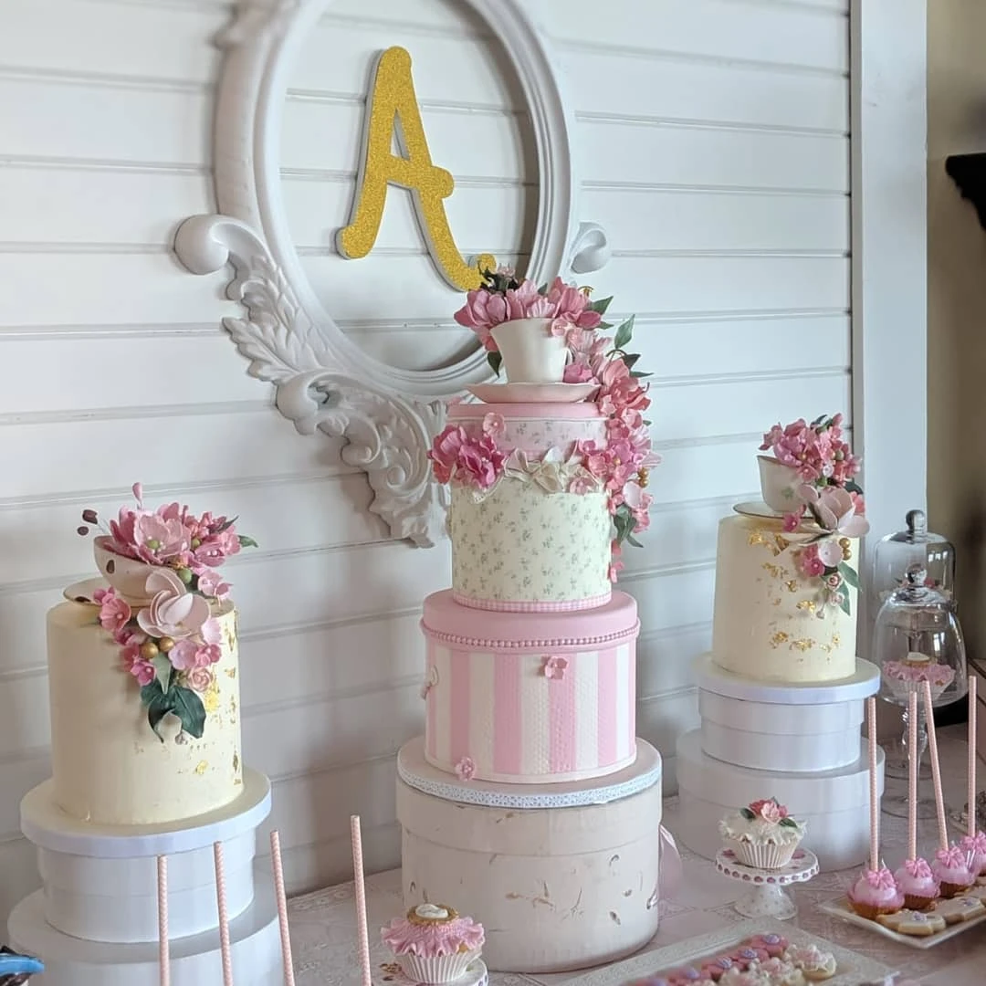 Elegant tea party bridal shower dessert table with multiple pink and white cakes decorated with flowers.