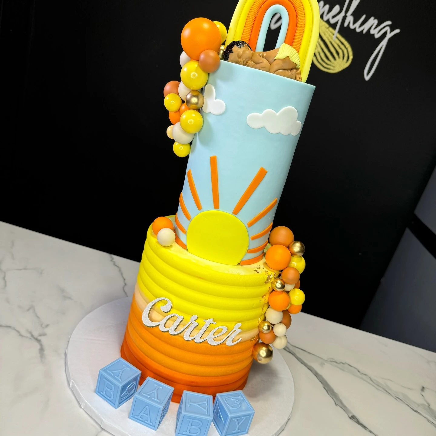 A two-tiered 'Here Comes the Sun' baby shower cake with sunrise ombre frosting and a sun motif.