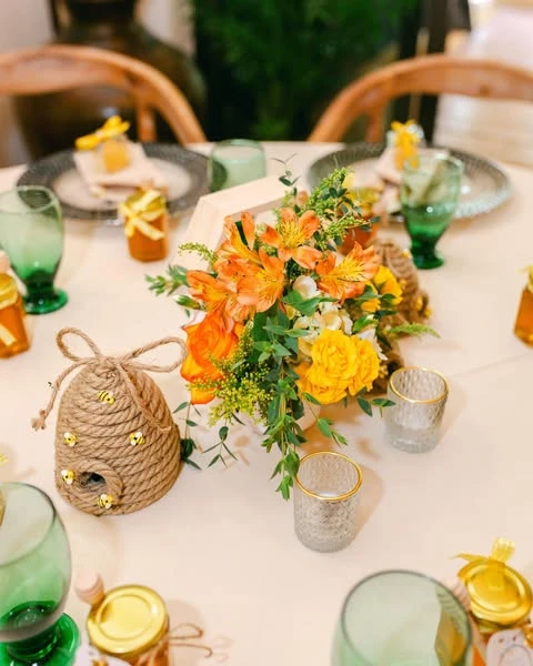 A 'Mommy-to-Bee' baby shower centerpiece with a twine beehive and a wooden box of orange and yellow flowers.