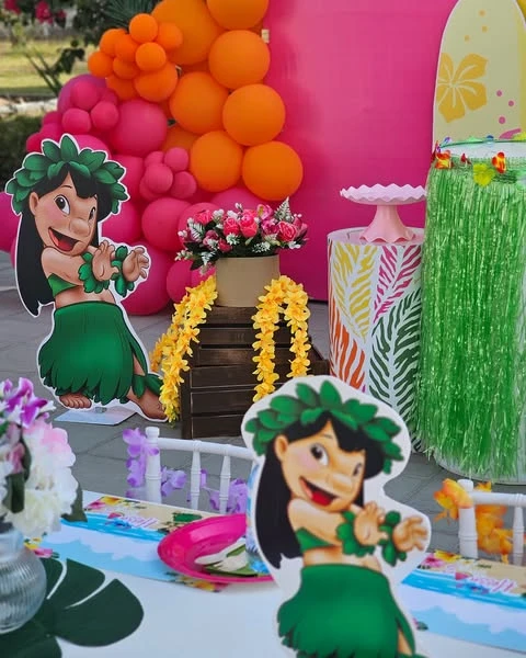 Lilo character cutouts at a Stitch-themed birthday party with a pink and orange balloon arch and yellow leis.