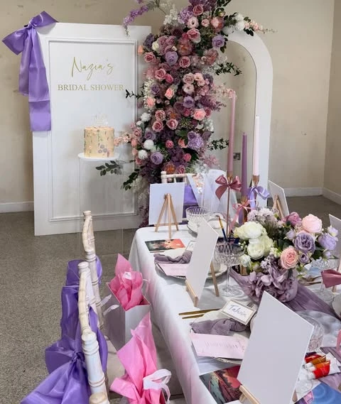 Spring bridal shower tablescape with purple and pink floral centerpieces that match the backdrop.