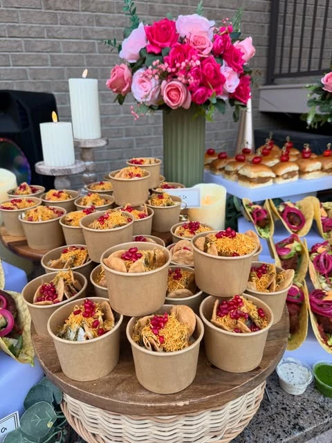Individual kraft paper cups filled with a savory snack mix and pomegranate seeds, arranged on a tiered stand.