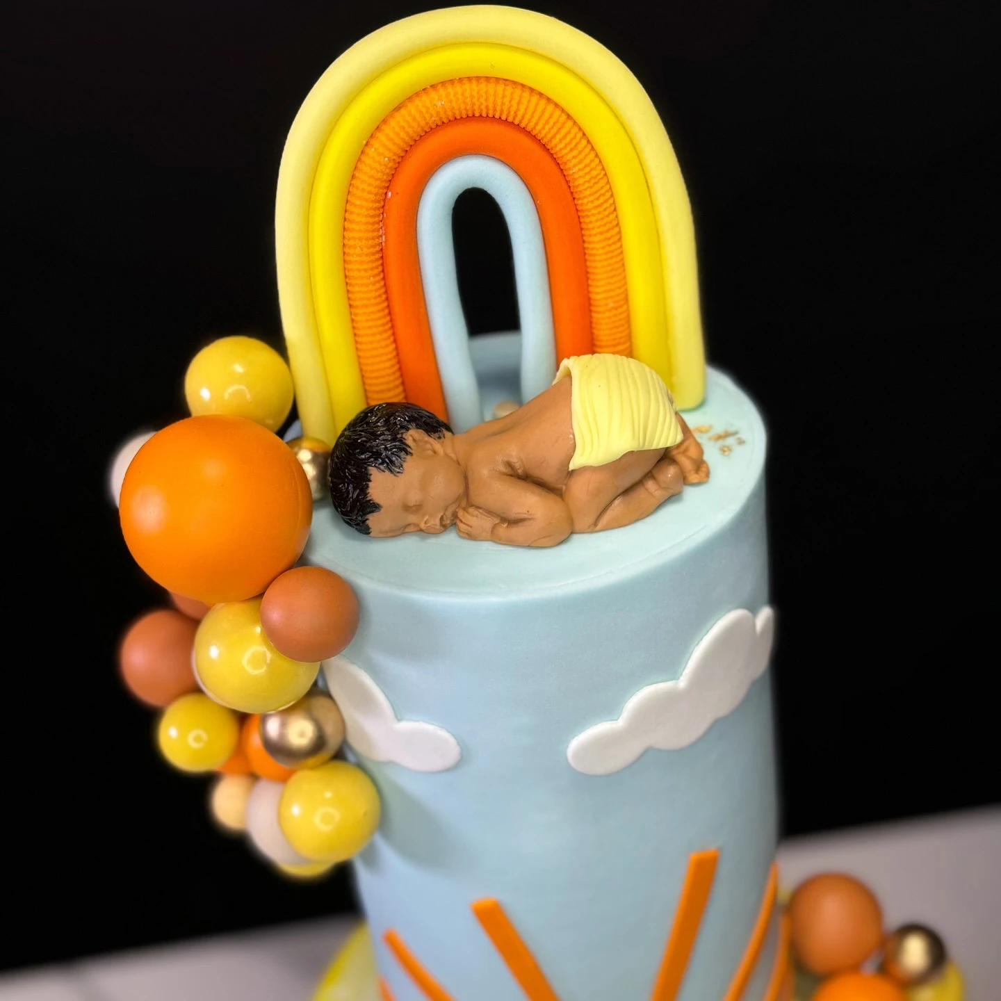 A of a fondant rainbow and sleeping baby figurine on top of a blue baby shower cake.