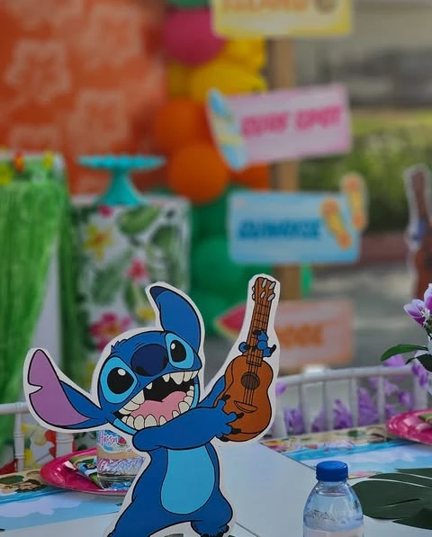A tabletop Stitch character cutout holding a ukulele at a tropical-themed party.