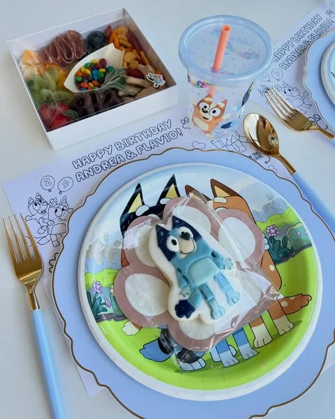 A complete Bluey-themed party place setting with a character plate, custom cookie favor, individual snack box, and coloring page placemat.