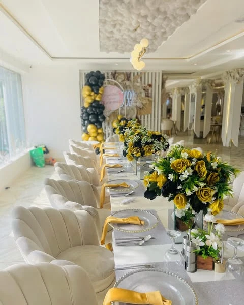 A long dining table set for a retirement party with gold napkins, beaded glass charger plates, and centerpieces of black and gold flowers.