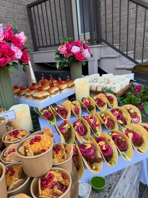 An angled view of a baby shower food bar featuring mini tacos, sliders, and individual snack cups.