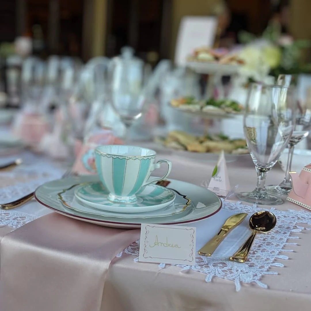 of a vintage tea party place setting with a striped teacup, gold flatware, and a lace doily.