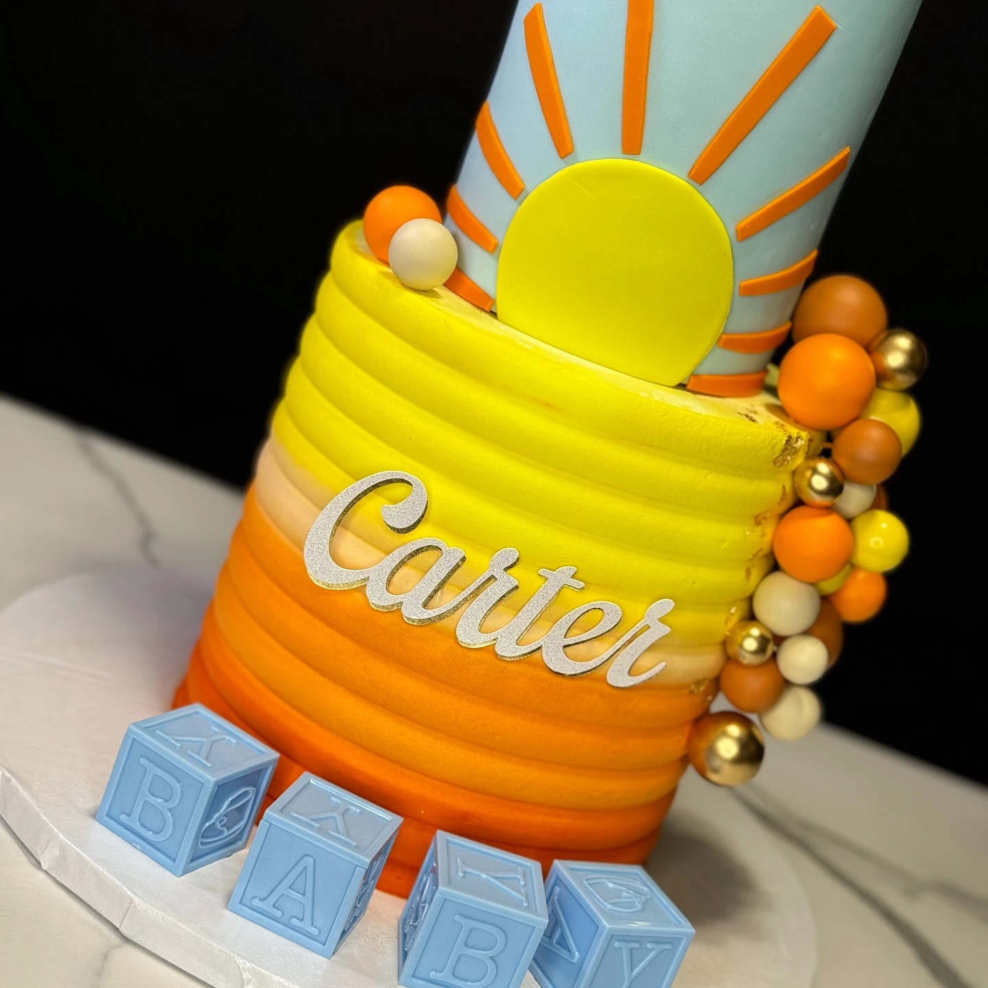Detail of a sunrise ombre frosting effect on a baby shower cake with a yellow sun decoration.