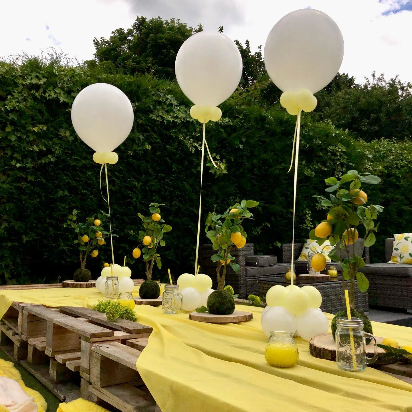 A baby shower table centerpiece featuring a small lemon tree on a wood slice with a tall white balloon floating above it.