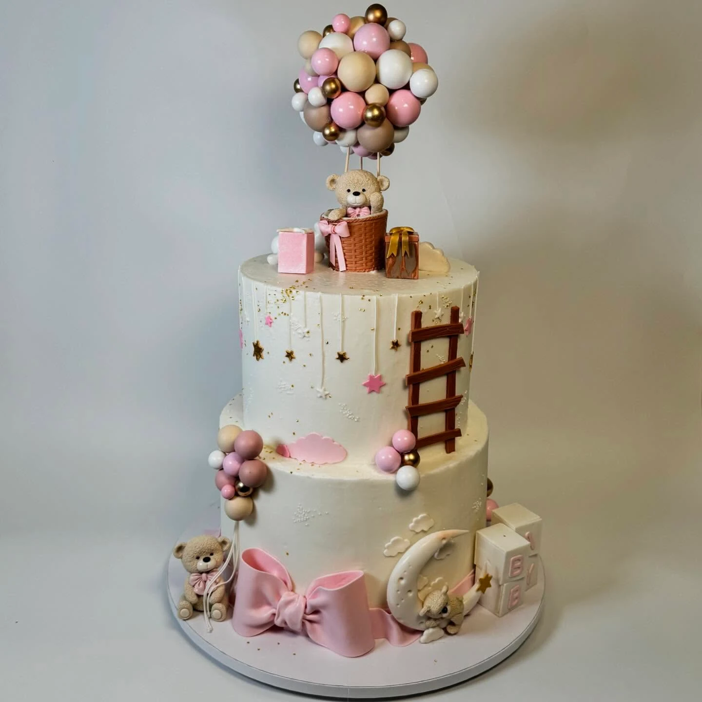 A two-tier 'we can barely wait' baby shower cake with a teddy bear in a hot air balloon topper.
