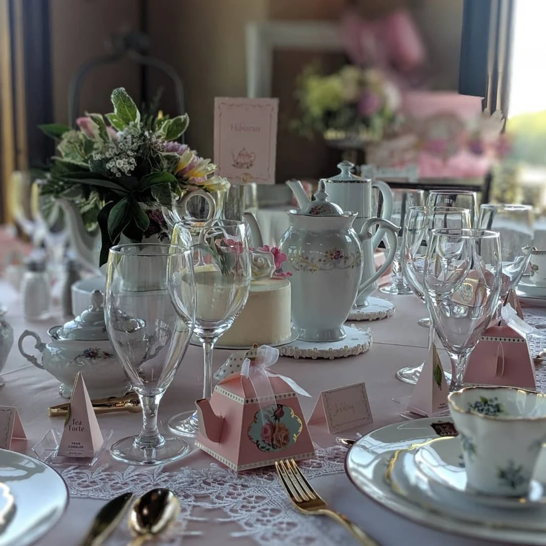Full view of a tea party bridal shower table set with vintage teapots, floral china, and party favors.