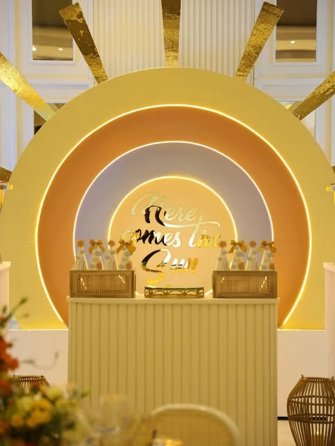 A 'Here comes the sun' baby shower dessert table with a large, layered sun and rainbow-themed backdrop.