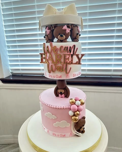 Two-tiered 'We can barely wait' baby shower cake with fondant teddy bears and a carousel top.