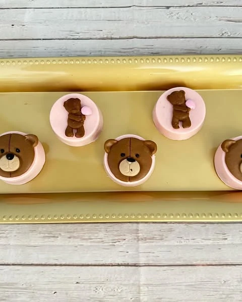 Pink chocolate-covered cookies with teddy bear decorations on a gold tray.