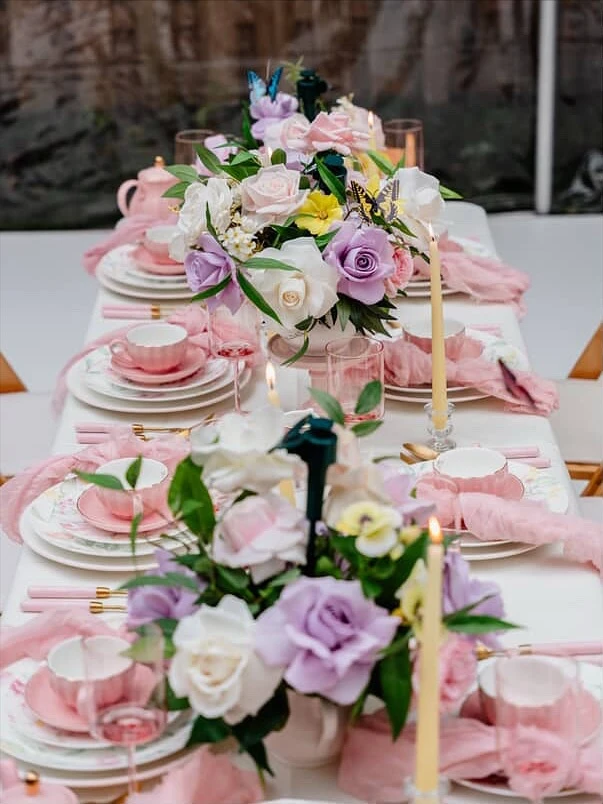 A long tea party bridal shower tablescape with pink teacups, pastel floral centerpieces, and taper candles.