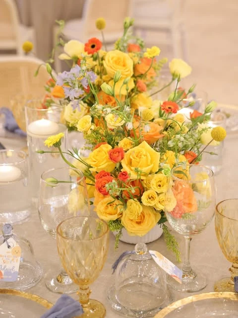 A baby shower floral centerpiece with yellow roses, orange flowers, and yellow craspedia billy balls.