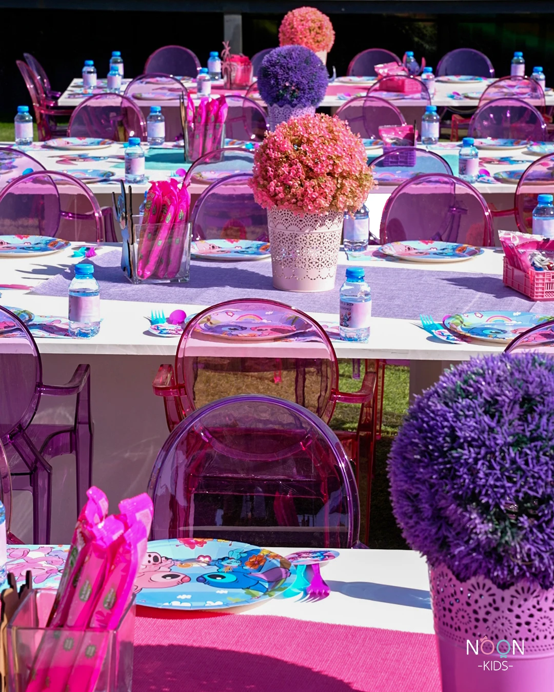 Long white tables decorated for a Stitch birthday party with purple and pink floral centerpieces.