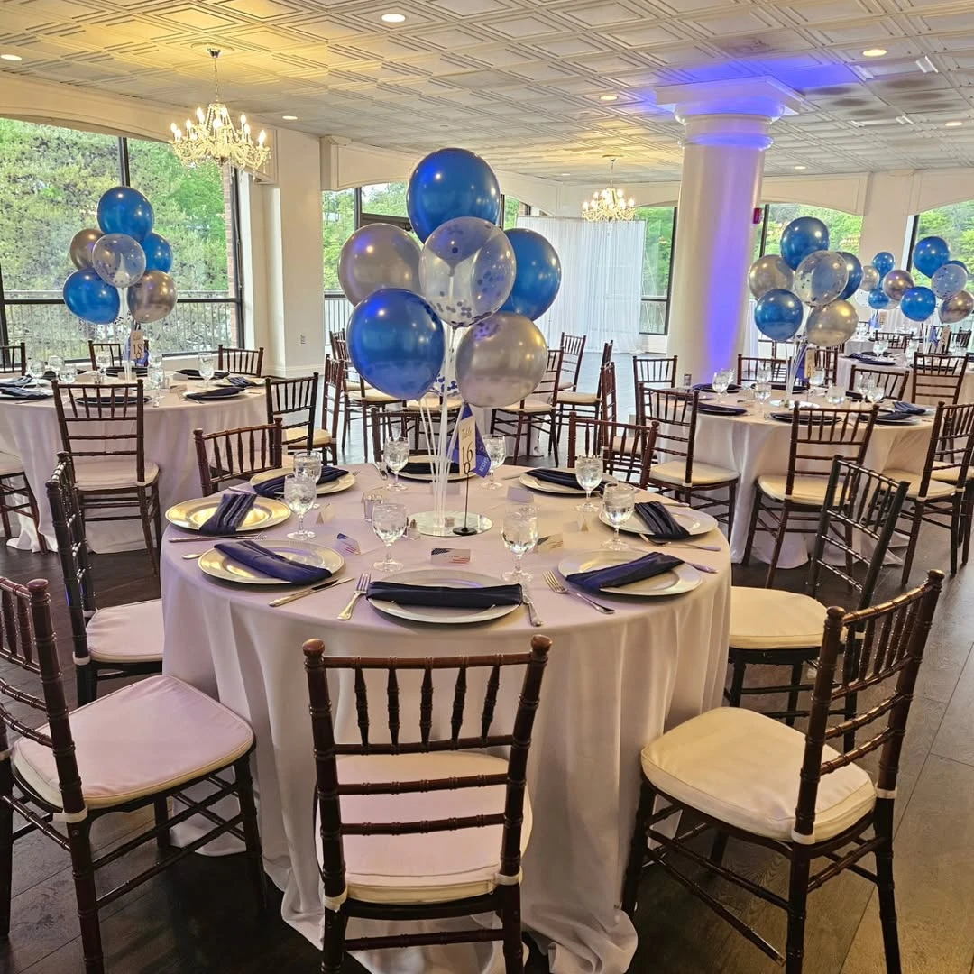 Banquet hall tables set for a retirement party with blue and silver balloon centerpieces.