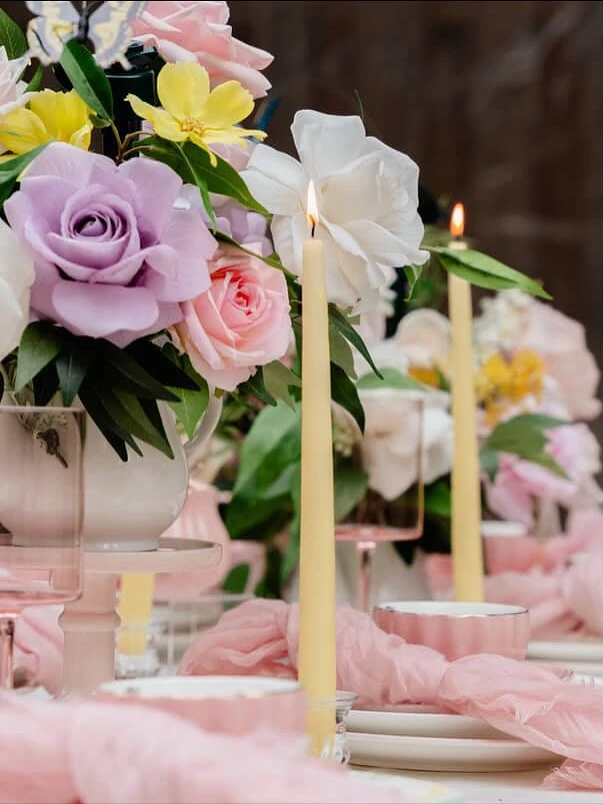A of a tea party centerpiece with lavender and pink roses next to a lit taper candle.