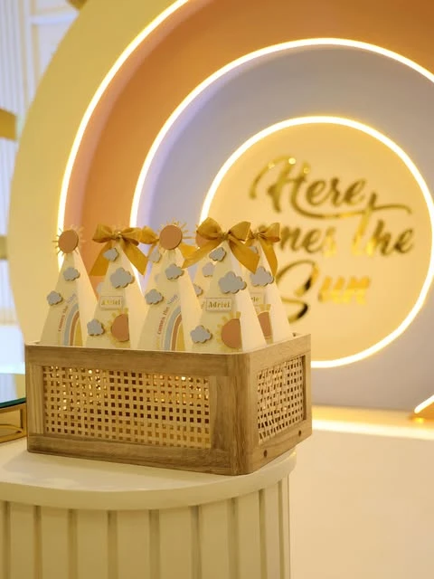 'Here comes the sun' themed party favor boxes displayed in a wooden and rattan basket.