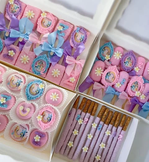 Assortment of Bluey-themed desserts including pink cakesicles and purple chocolate-covered pretzels.