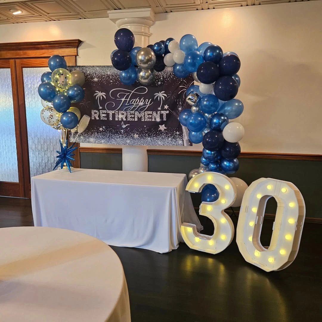 A 'Happy Retirement' banner with a balloon arch and light-up marquee numbers spelling '30' for years of service.