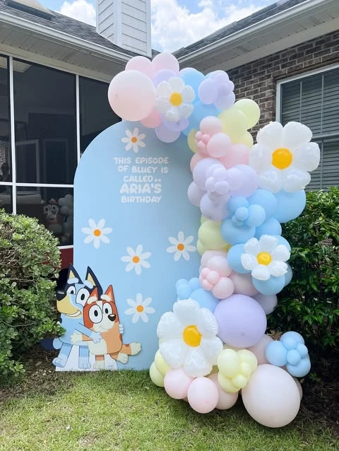 A Bluey-themed birthday party photo backdrop with a pastel balloon arch and character cutouts.