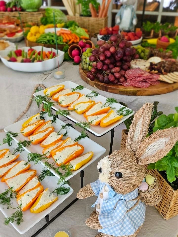 A Peter Rabbit themed baby shower food table featuring a straw rabbit figurine next to tiered plates of cheese-stuffed mini peppers.
