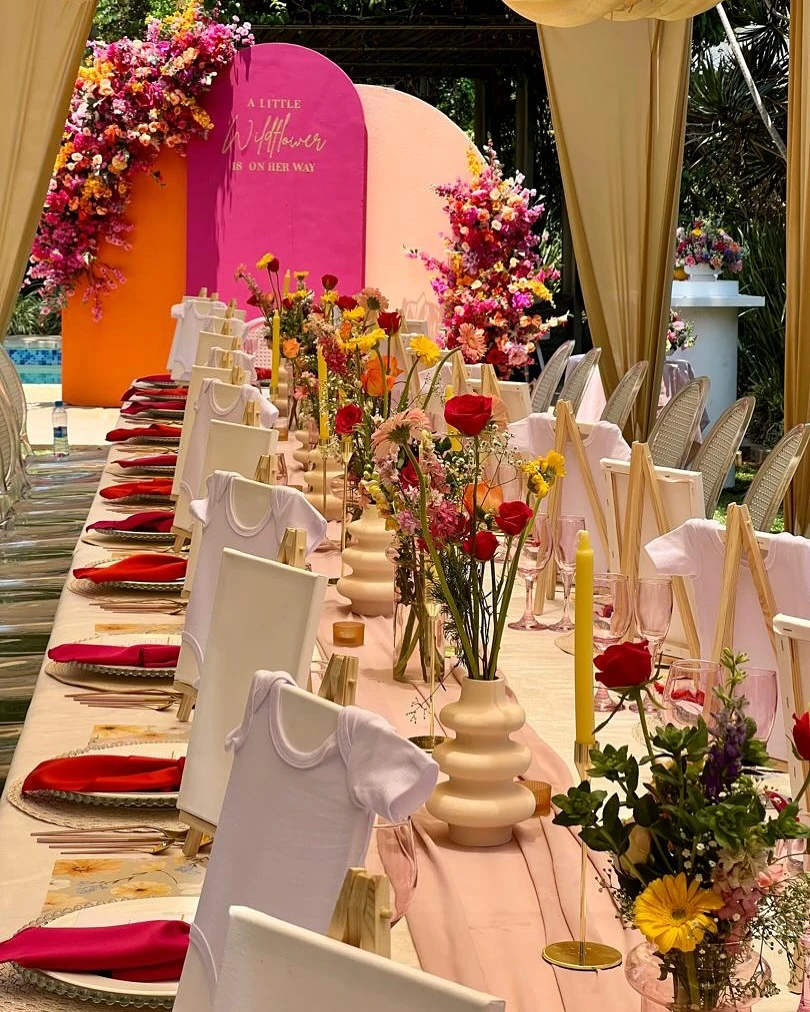 A modern wildflower baby shower theme with a bold pink and orange backdrop and a long, decorated guest table.