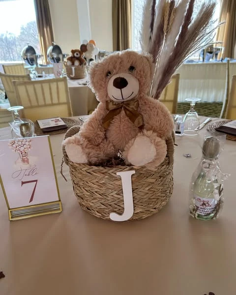 A teddy bear centerpiece in a woven basket with a white initial 'J' on a baby shower table.