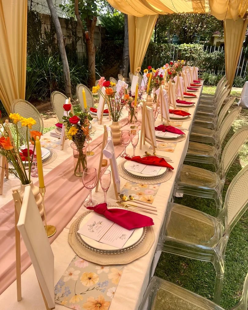 A long table set for a wildflower baby shower with colorful floral centerpieces and pink napkins.