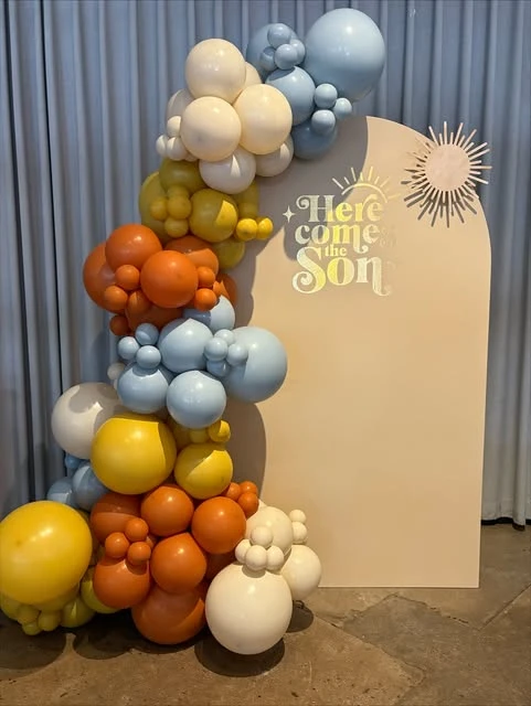 Here Comes the Son baby shower backdrop with a colorful balloon garland.