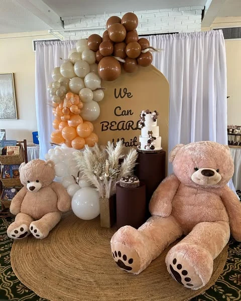 'We Can Bearly Wait' baby shower backdrop with large teddy bears, balloons, and cake stands.