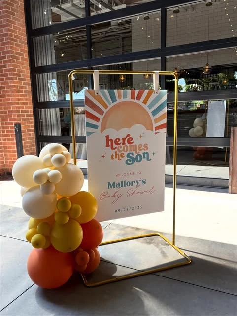 Here Comes the Son baby shower welcome sign on a gold stand.