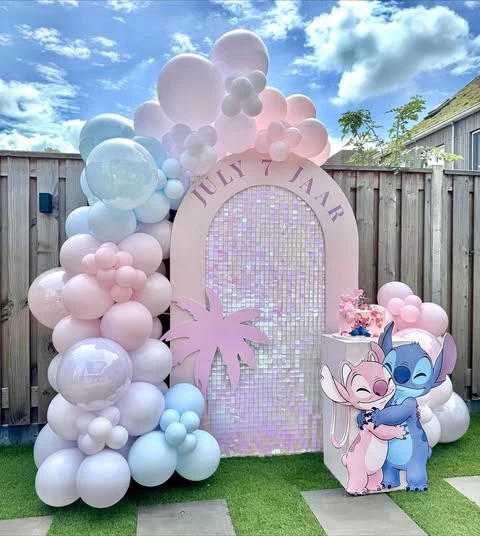 Side view of a Stitch and Angel birthday party backdrop, showing the depth of the pastel balloon arch against an iridescent shimmer wall.