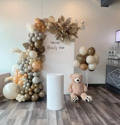 Neutral balloon arch backdrop for a 'we can bearly wait' baby shower with a teddy bear.